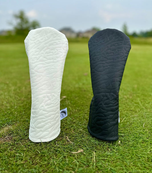 White and black golf club headcovers on a grassy background