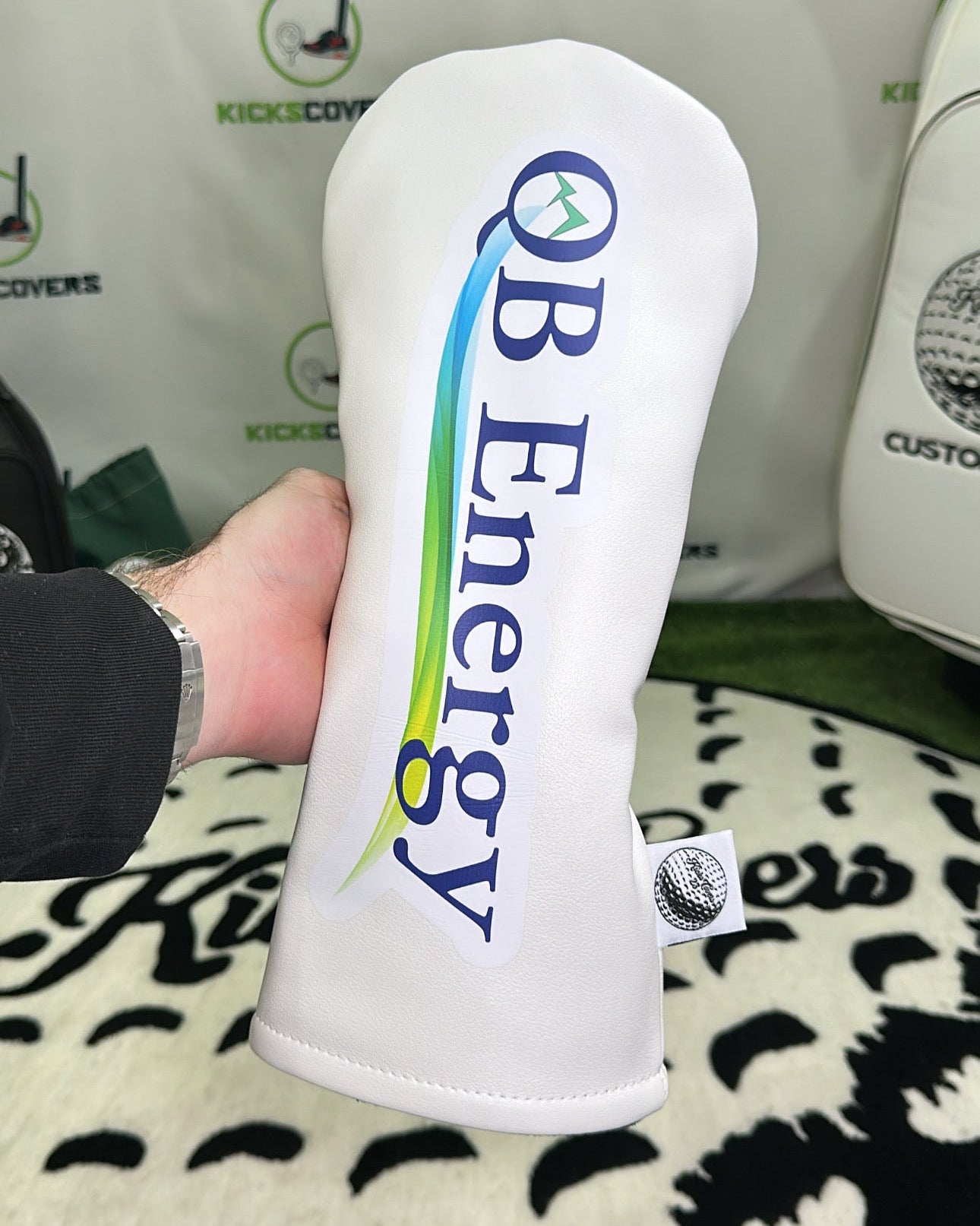 Golf club head cover with 'OB Energy' branding on a patterned surface.