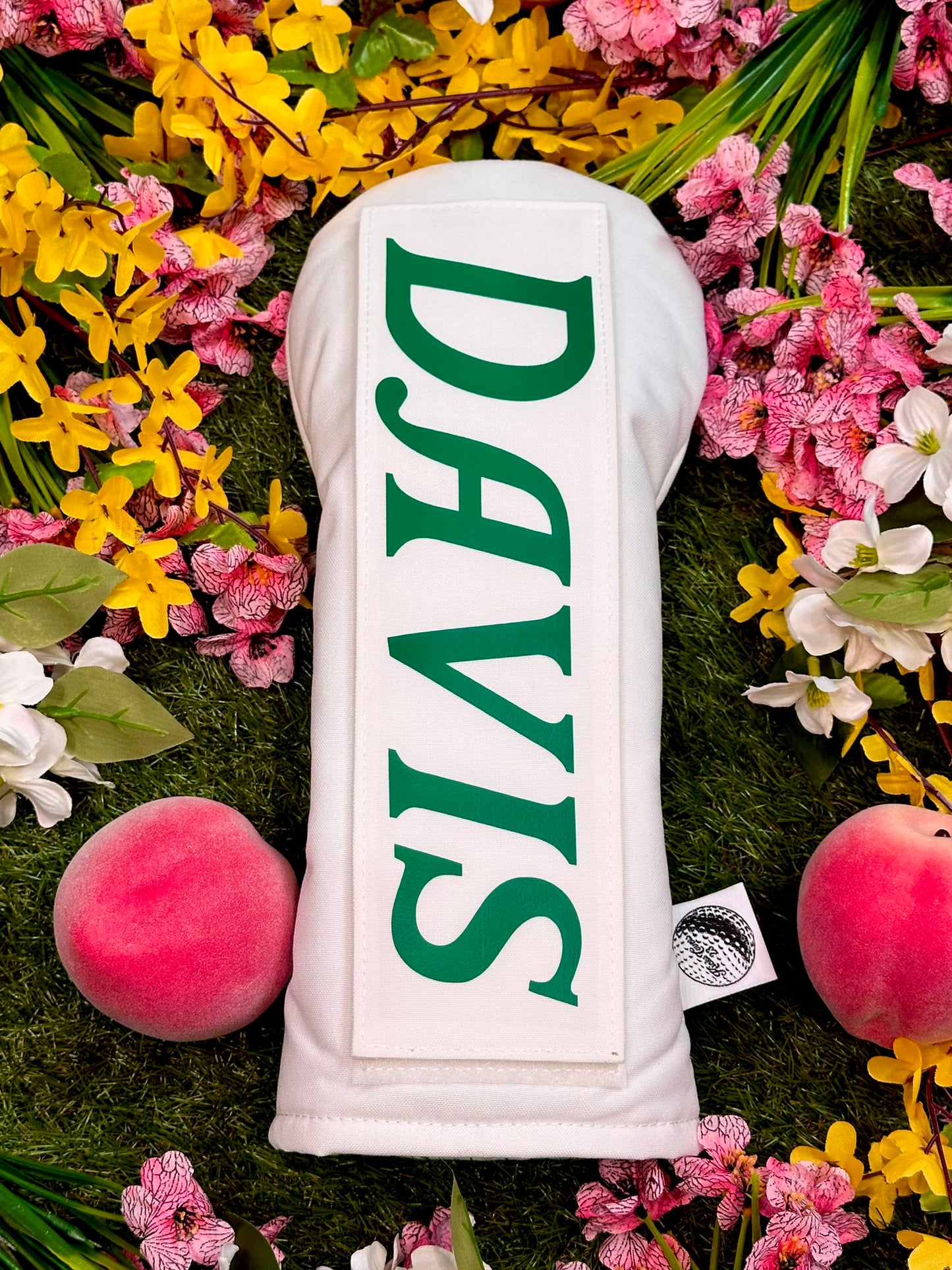 White golf club head cover with 'DAVIS' branding on a grassy background with flowers