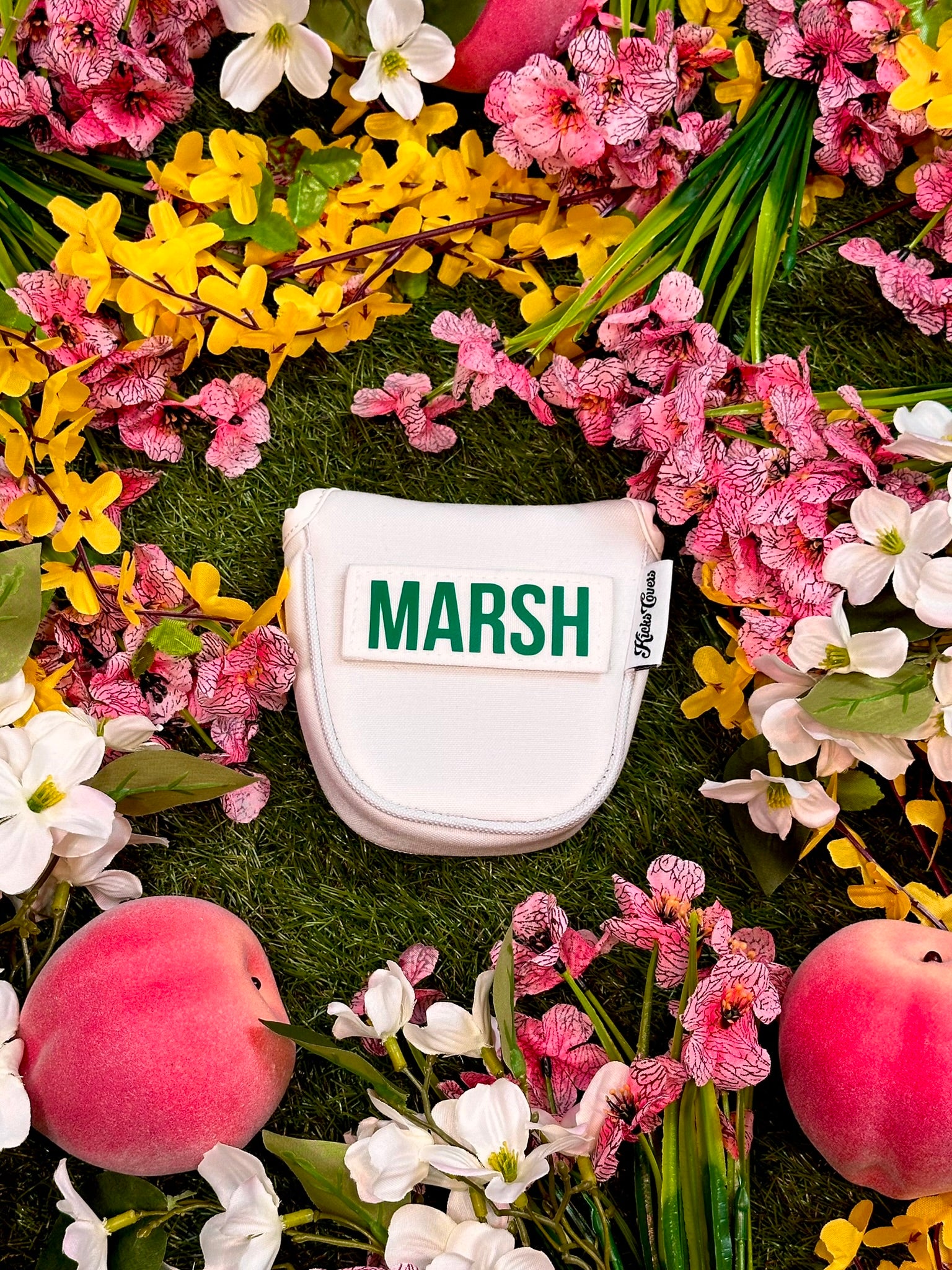 White putter cover with 'MARSH' branding surrounded by colorful flowers and fruits on a green background