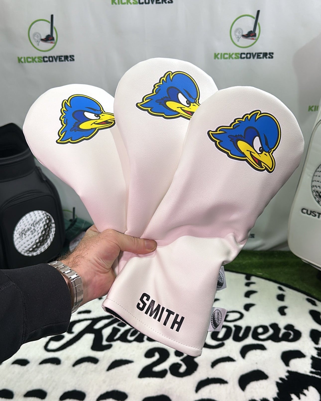 Three golf club heads with blue duck logo and 'Smith' branding on a black and white patterned surface.