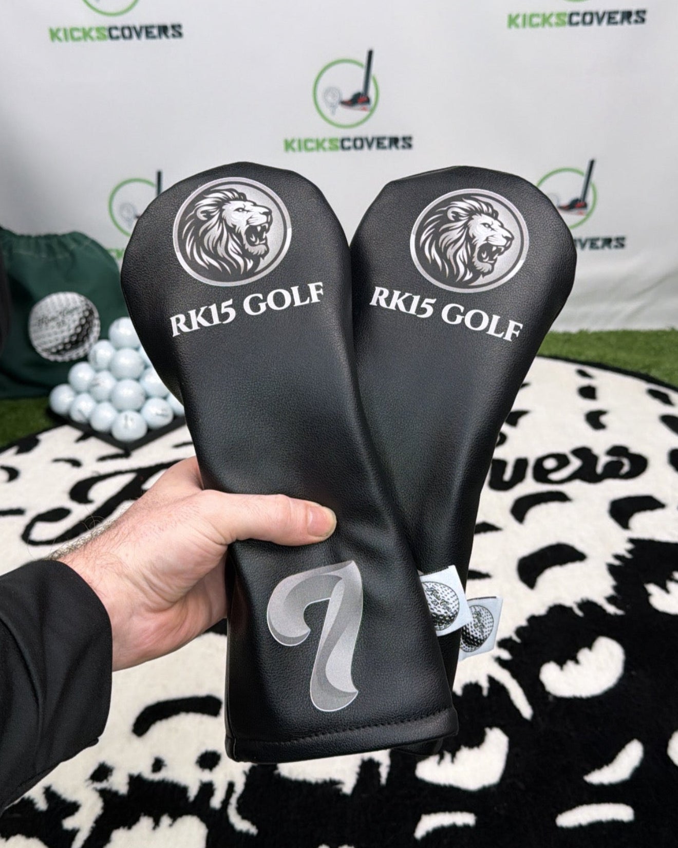 Two golf club covers with 'RK15 GOLF' branding held by a person, against a branded backdrop.