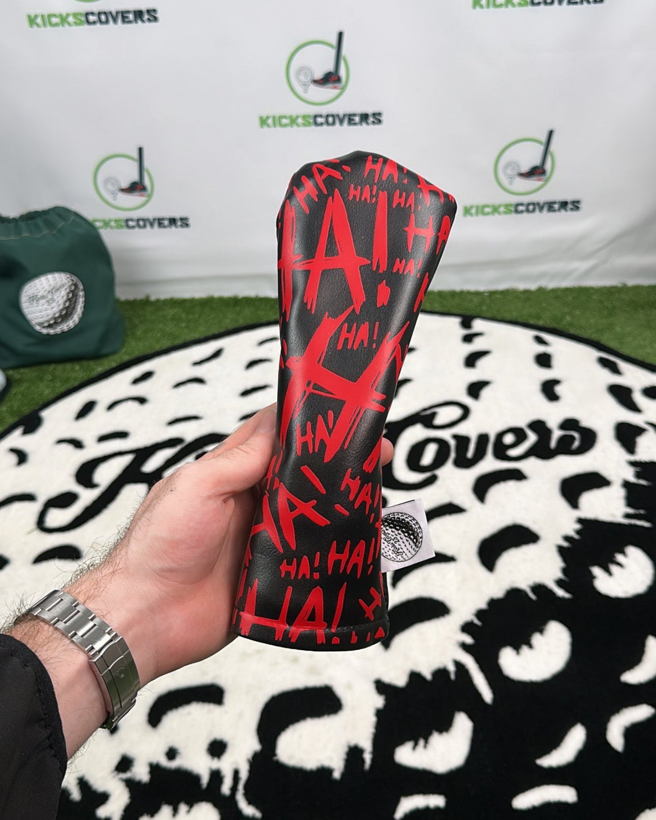 Person holding a red and black golf club head cover with 'KicksCovers' branding in the background.