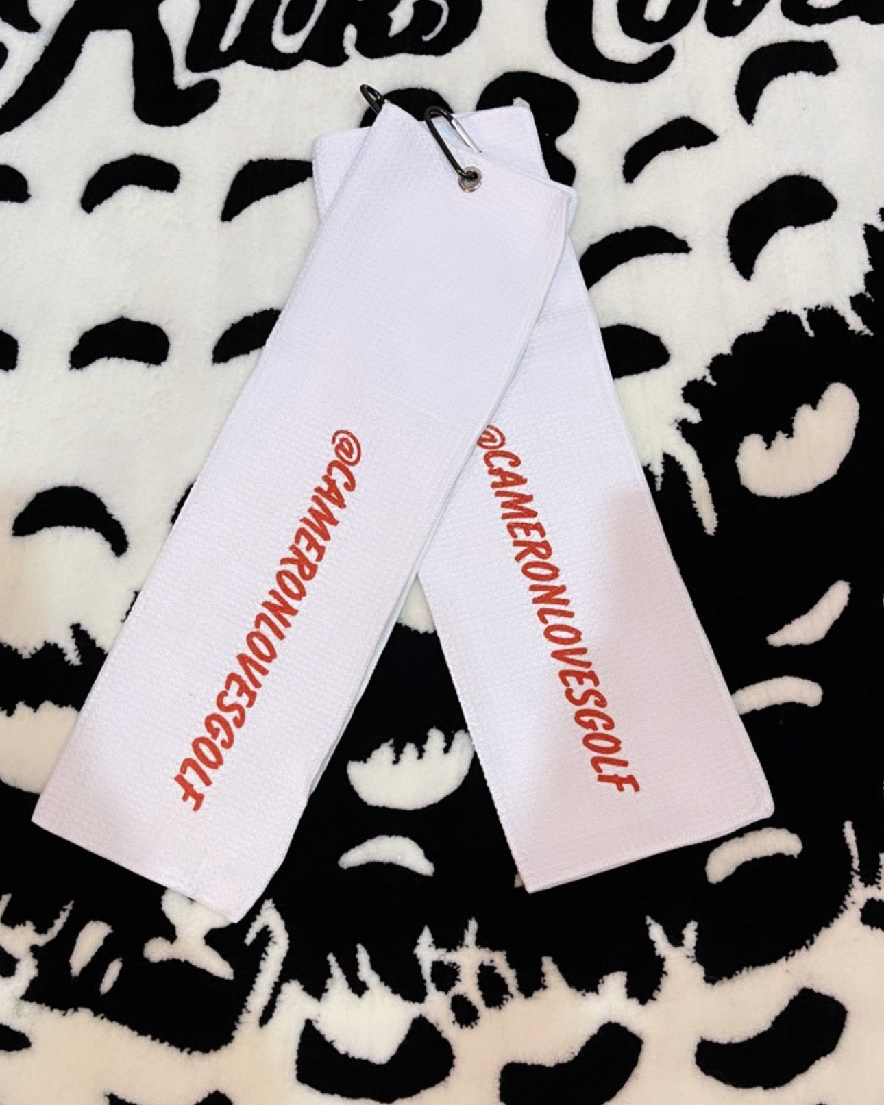 Two custom golf towels with branding on a patterned towel background.