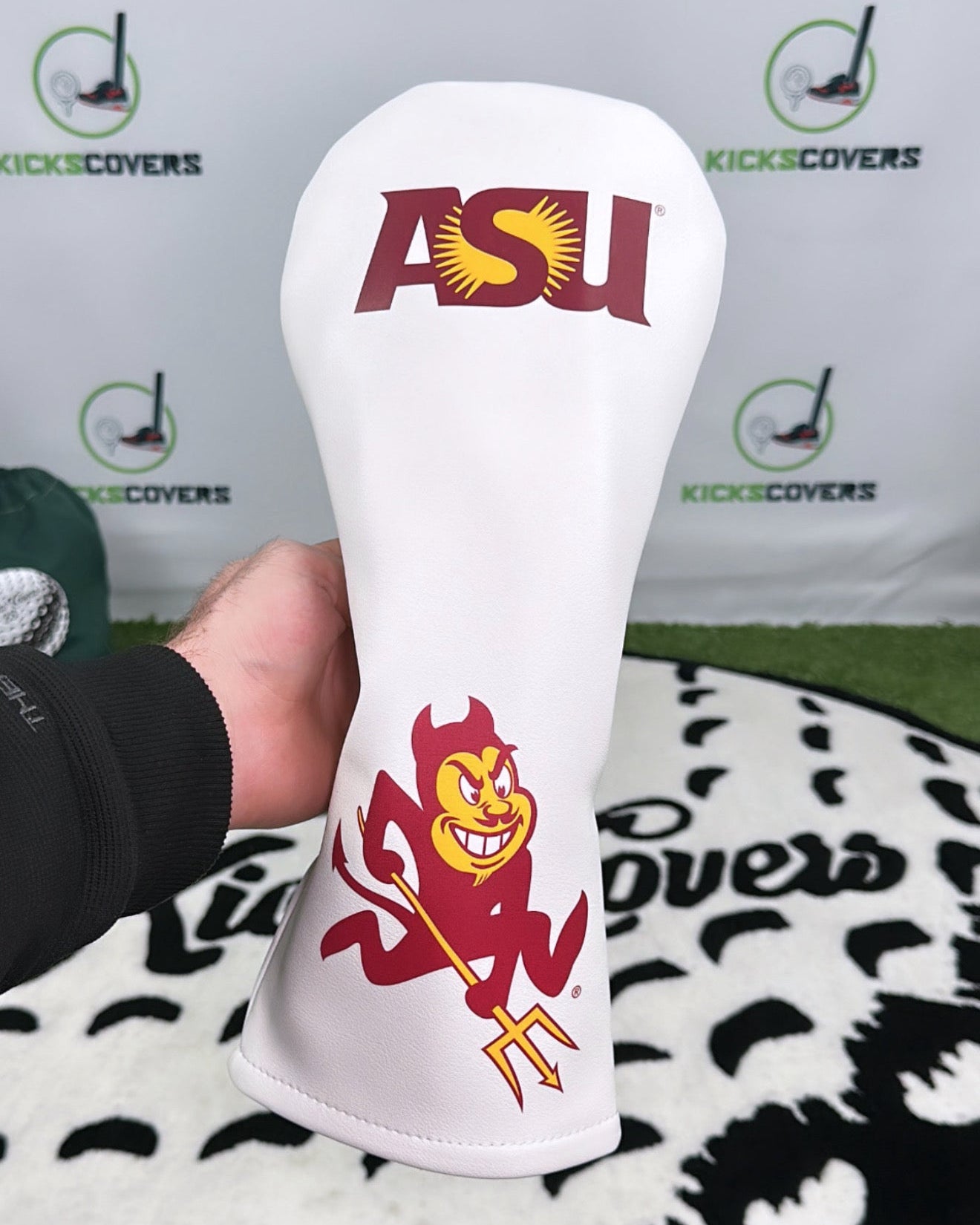 White golf head cover with ASU logo held in front of a branded background