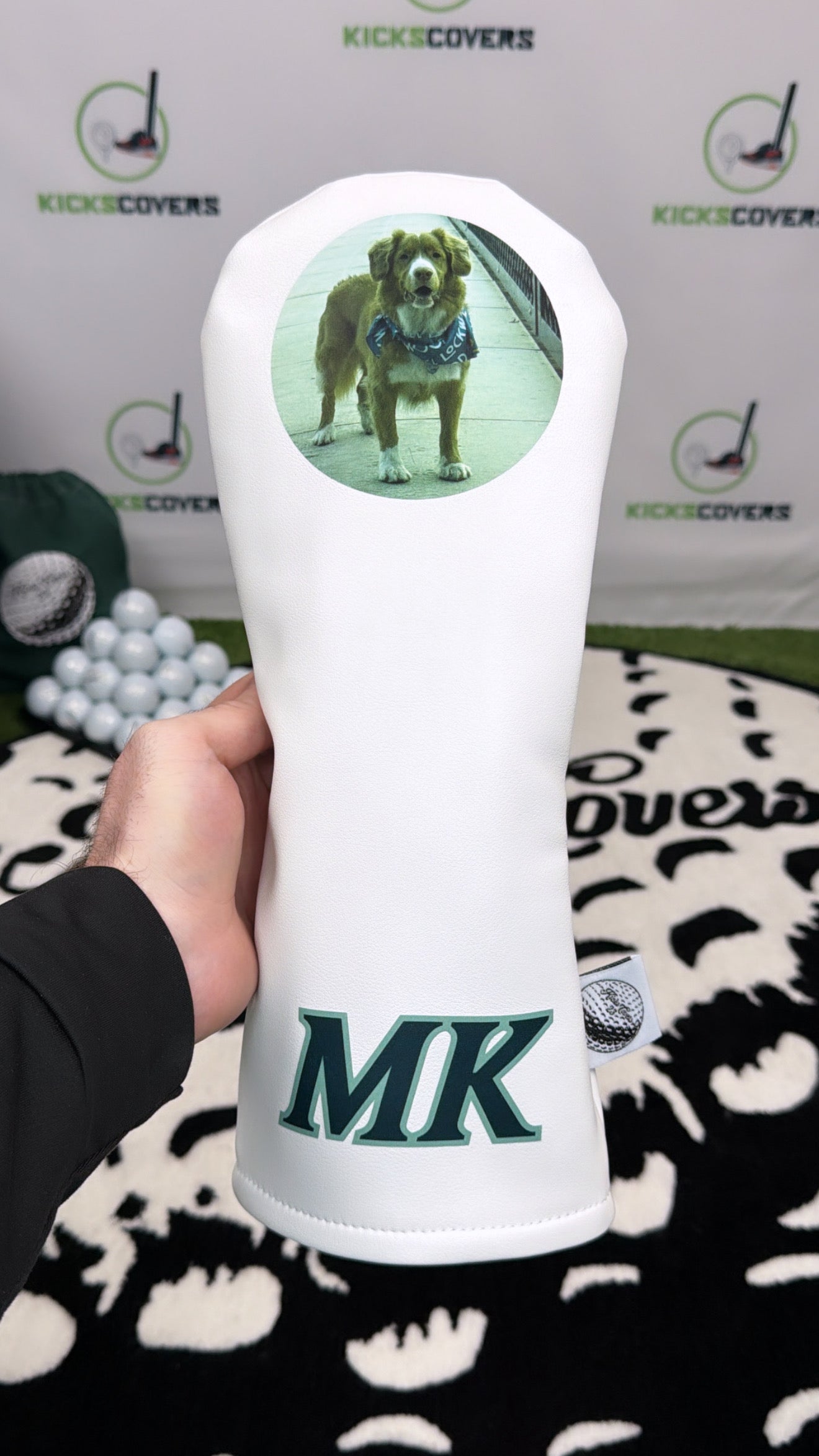 White golf club head cover with a dog design and 'MK' branding, held by a person.