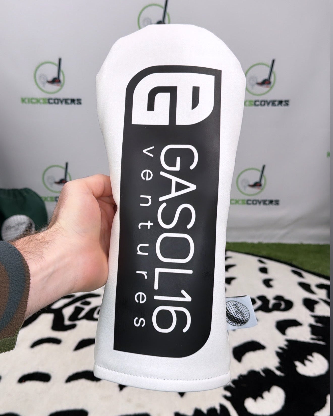 White and black golf club head cover with 'Gasol16 Ventures' branding held by a hand.